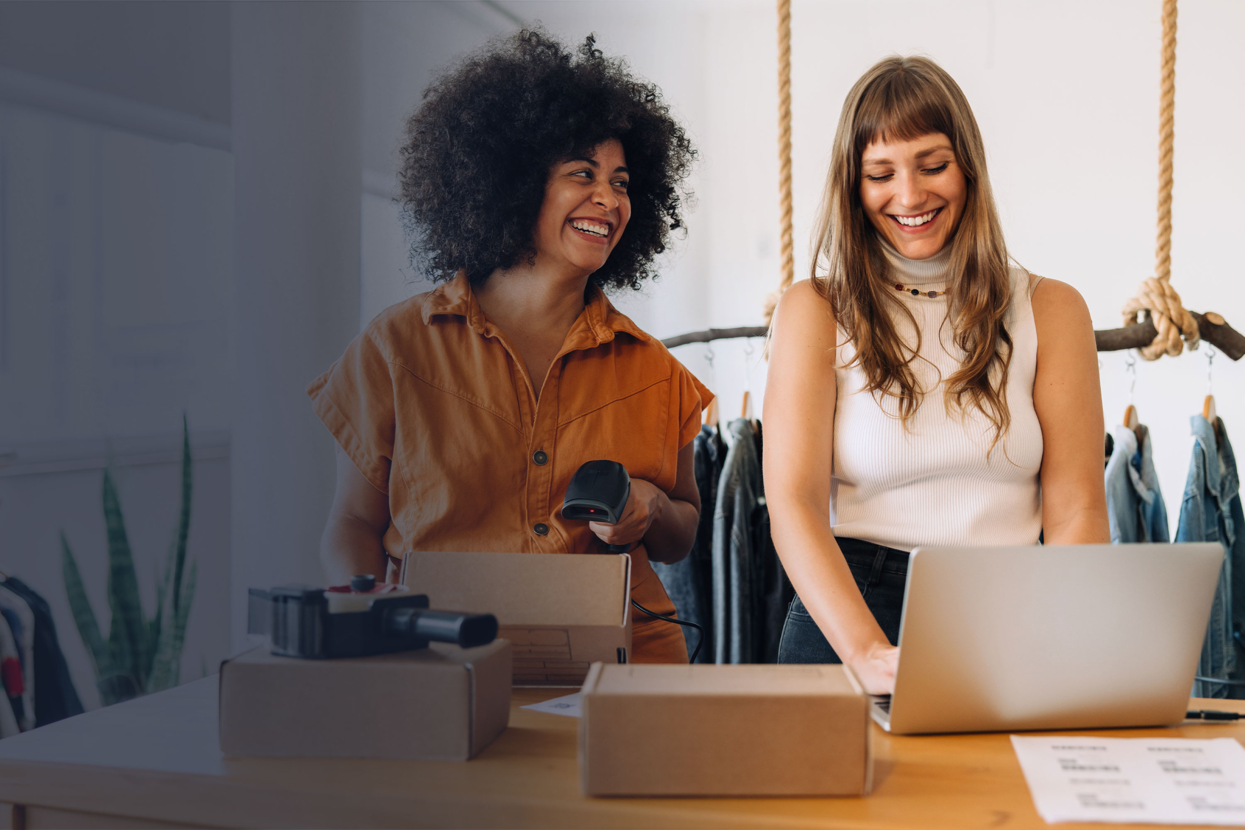 Zwei Frauen arbeiten in einem Modegeschäft am Verkaufstresen mit Laptop und Barcode-Scanner