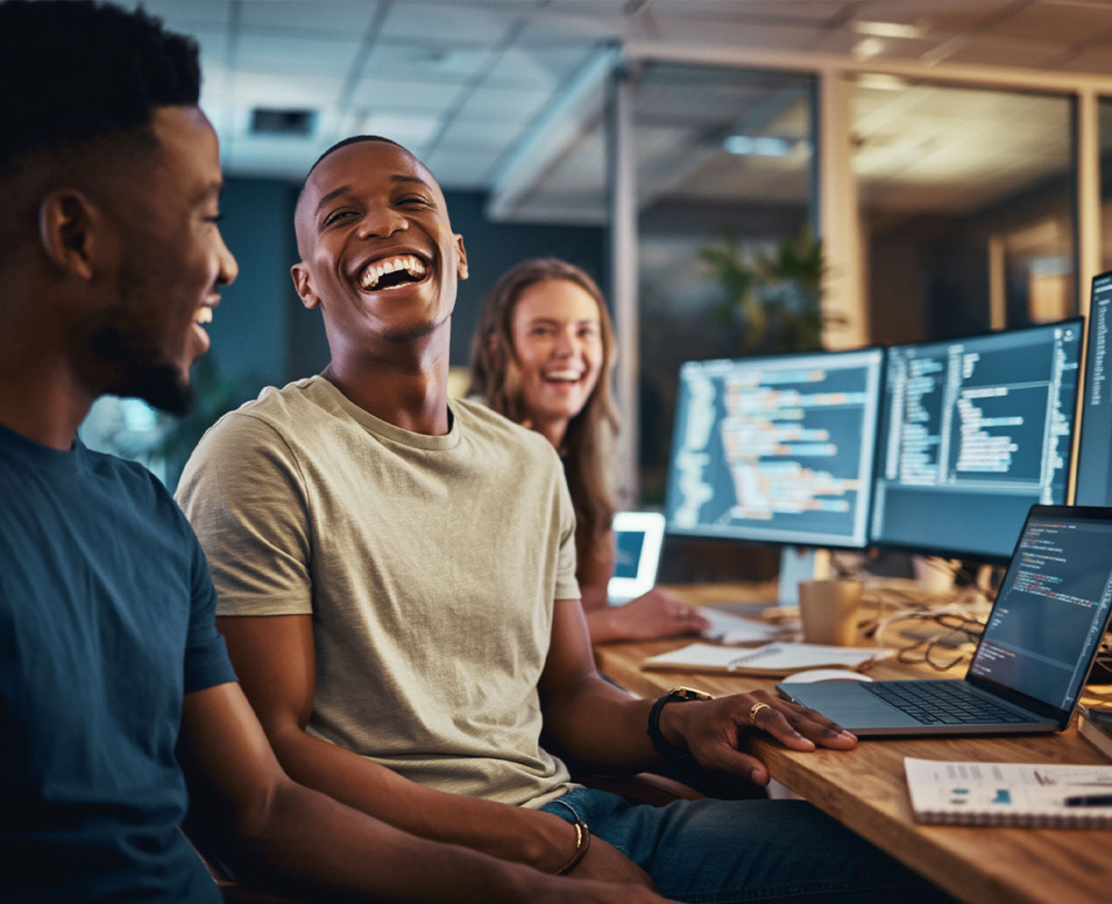 Drei lachende Software-Entwickler bei der Arbeit an Monitoren mit Programmcode